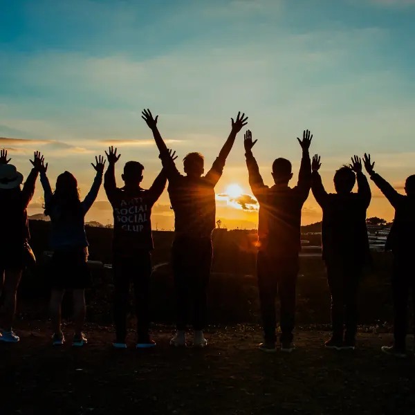 Grupo de pessoas de braços erguidos diante do pôr do sol